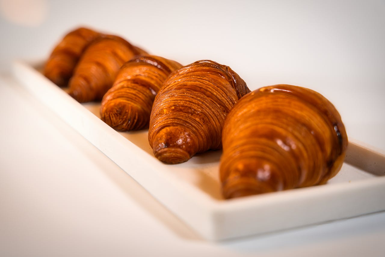 A row of freshly baked artisanal croissants displayed on a white ceramic plate.