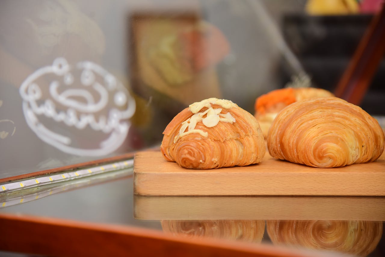 Delicious freshly baked croissants topped with almonds on a wooden board in a bakery display.